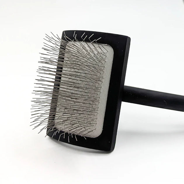 Pet grooming brush with black handle and clear bristle design on a white background